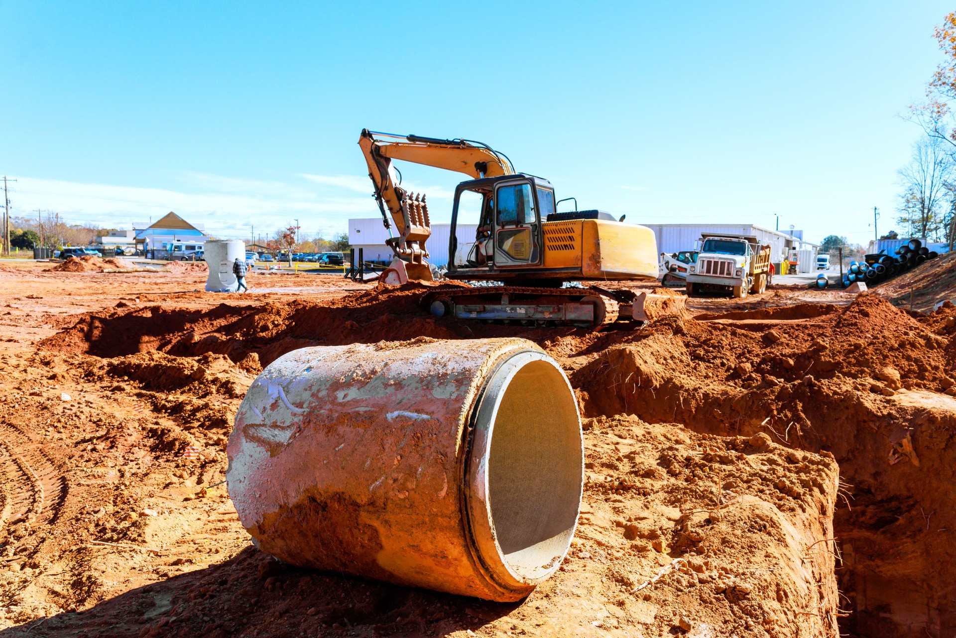 Construction work takes place on a sunny day with heavy machinery operating on a dirt site